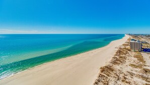 Une plage aux eaux d’un bleu limpide et au rivage sablonneux. Des bâtiments bordent la côte.