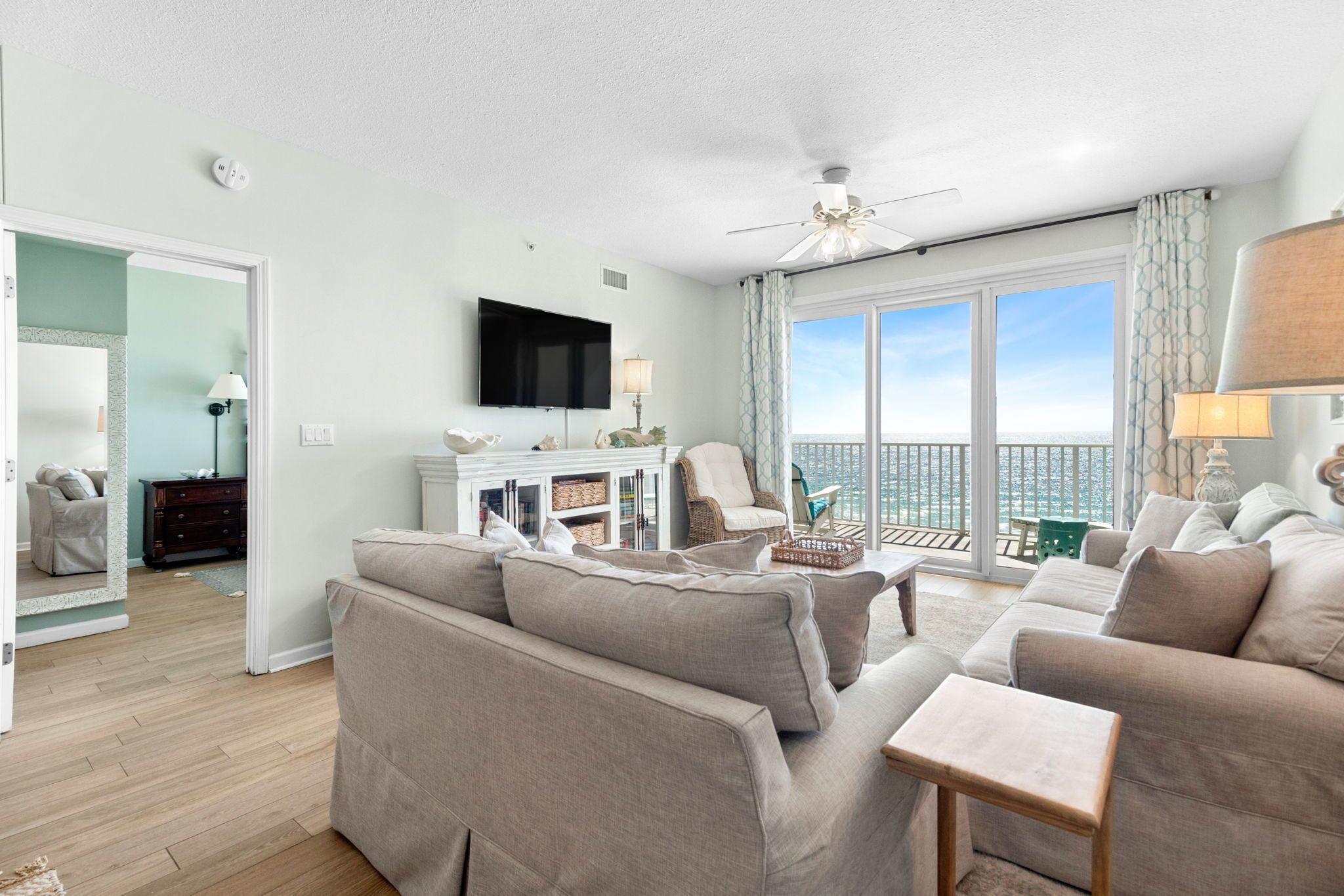 A spacious living room with a large sofa, a coffee table, and a TV. There is a balcony with a view of the city.