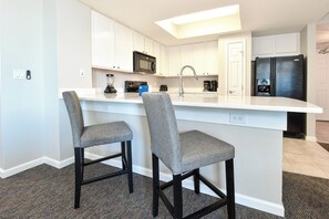 A modern kitchen with white cabinets, a black refrigerator, a microwave, and a bar area with two grey chairs.