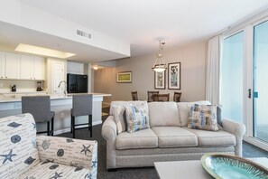 A modern living room with a sofa, chairs, a coffee table, and a kitchen area with cabinets and appliances.
