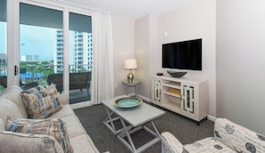 Een moderne woonkamer met een bank, een salontafel, een televisie en een balkon met uitzicht op hoge gebouwen.