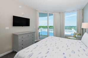 A hotel room with a bed, a dresser, a television mounted on the wall, and a view of a pool and greenery outside.