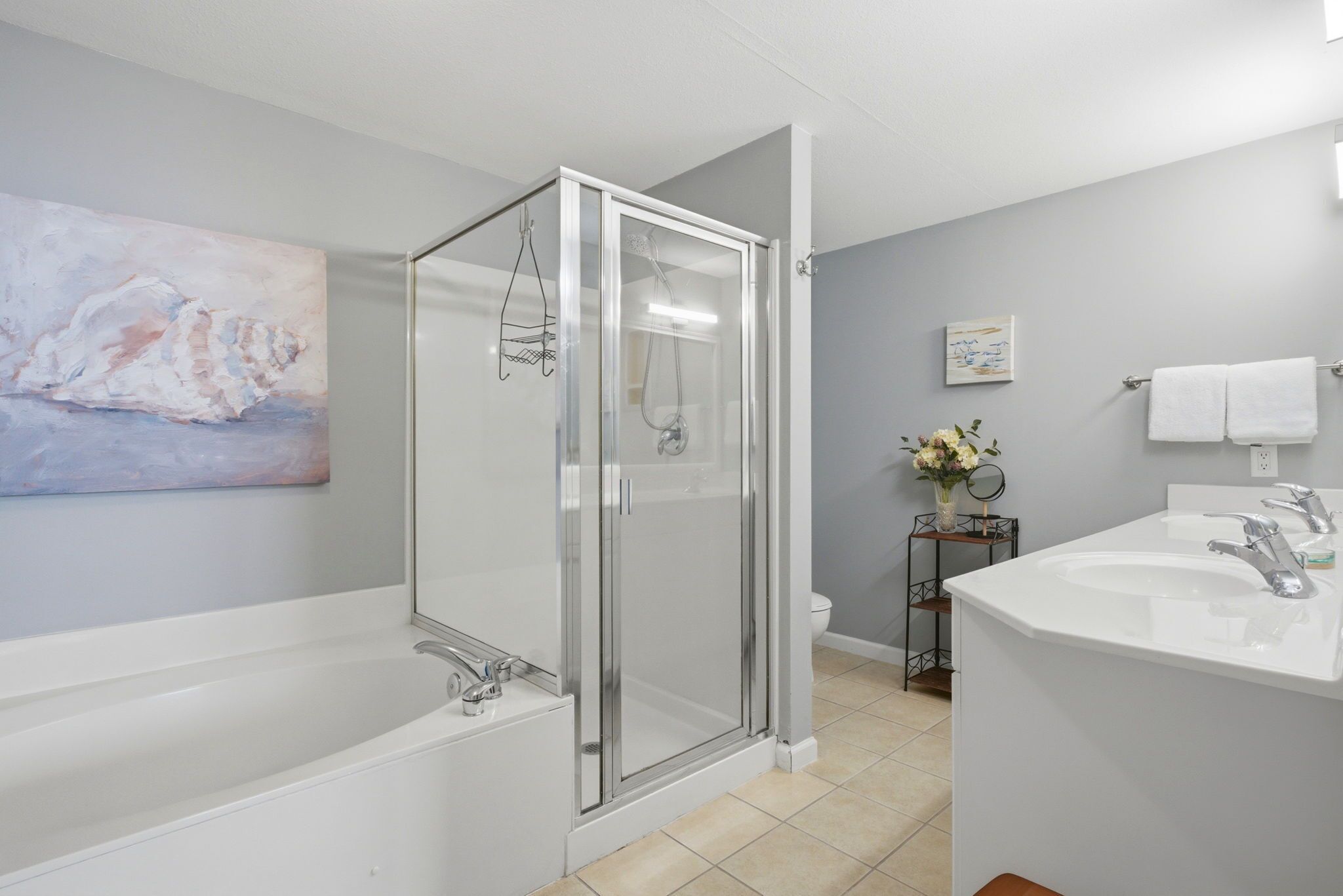 Un baño moderno con ducha envuelta en vidrio, una bañera blanca, un lavabo con espejo y un inodoro.