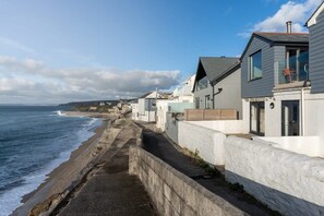 Uma área residencial costeira com casas junto ao mar, apresentando uma passagem estreita e um muro de pedra.