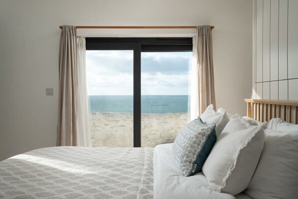 A bedroom with a bed, a view of the beach, and a window with curtains.