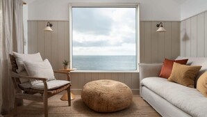Une pièce dotée d’une grande fenêtre, d’un canapé, d’un fauteuil, d’une petite table et de deux lampes fixées au mur.