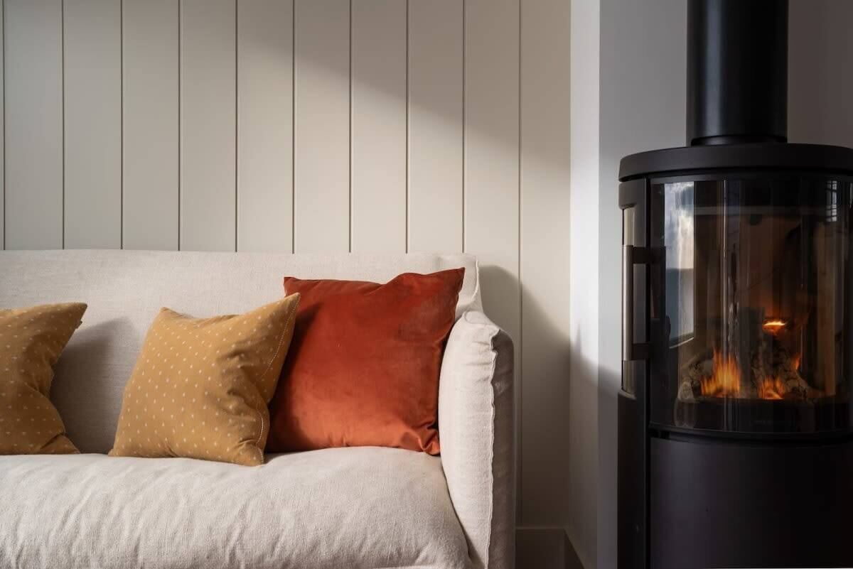 A room with a sofa, pillows, and a wood-burning stove.