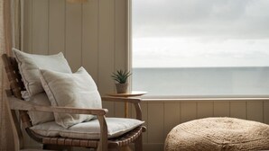 Une pièce d’angle avec une chaise en bois, une petite table ronde ornée d’une plante et une vue sur la mer.