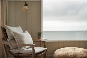 A corner room with a wooden chair, a small round table with a plant, and a view of the sea.