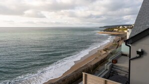 Une vue sur la côte, depuis un balcon donnant sur une plage avec des vagues, un mur de pierre et un bâtiment doté d’un toit en pente.
