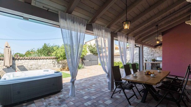 Un patio cubierto con un jacuzzi, una mesa de comedor y sillas.