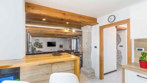 Una cocina moderna con vigas de madera, un pilar de piedra y un comedor con sillas blancas.