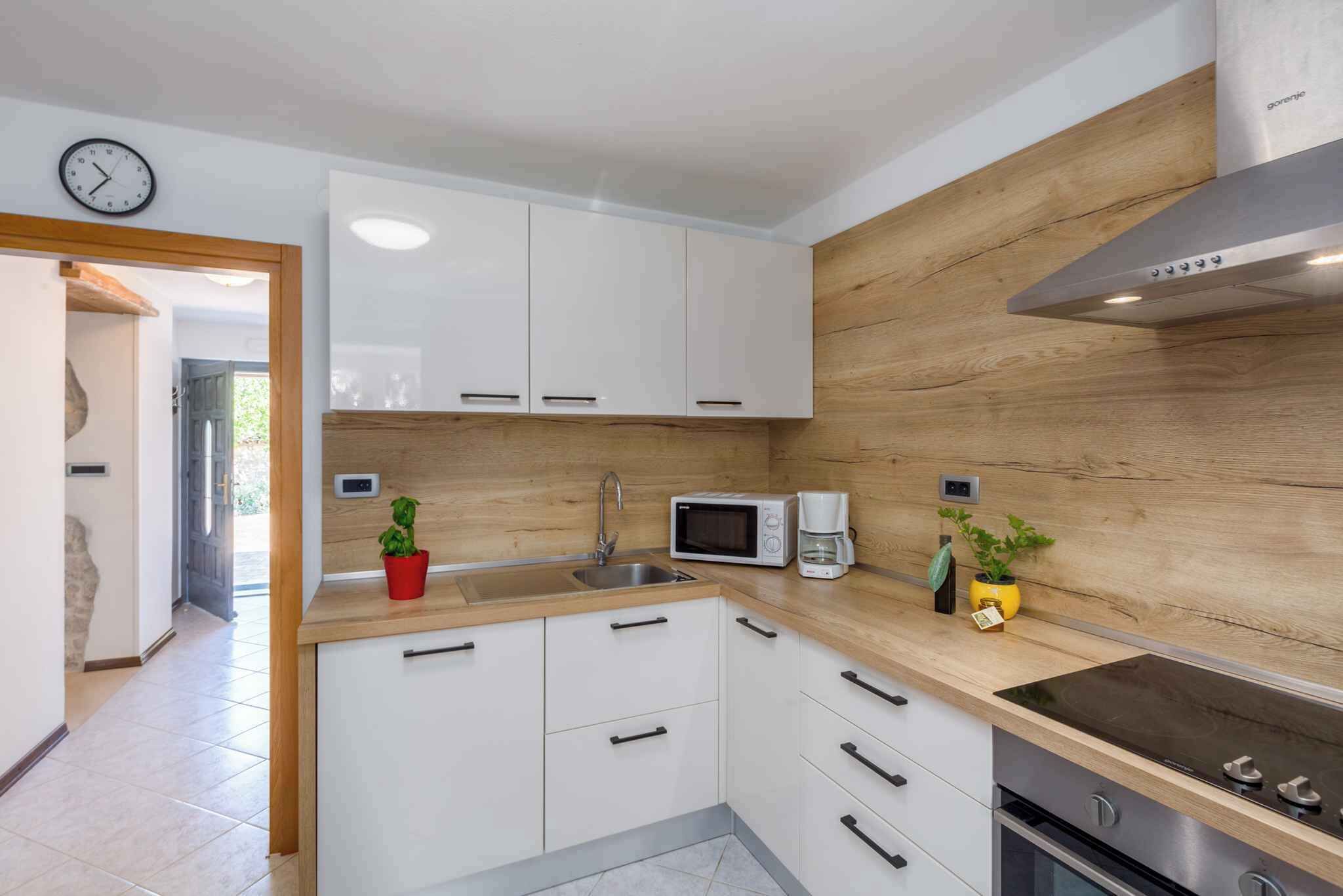 A modern kitchen with white cabinets, a wooden backsplash, a microwave, a coffee maker, and a stove.