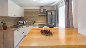 Una cocina moderna con armarios blancos, encimera de madera, refrigerador de acero inoxidable y una mesa de comedor con un bol de fruta.
