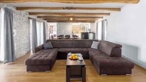 Una sala de estar moderna con un amplio sofá modular en forma de L, una mesa de centro de madera con fruta y vigas de madera a la vista en el techo.