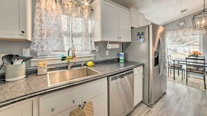 A modern kitchen with white cabinets, a stainless steel refrigerator, a dishwasher, and a window with floral curtains. - 1/2 Mi to Fort Campbell: 'State Line Retreat' (Clarksville)