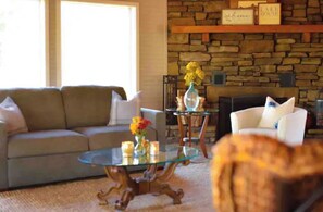 Relax in this inviting living room with a comfortable sofa, coffee table, and side table, accompanied by a fireplace and a beautiful vase of flowers.