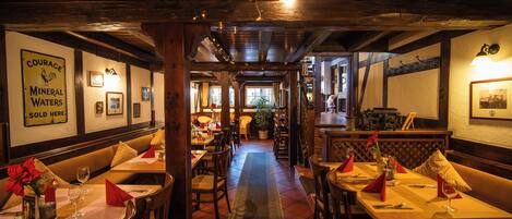 A restaurant with wooden beams, a central aisle, and tables set with red napkins and wine glasses.