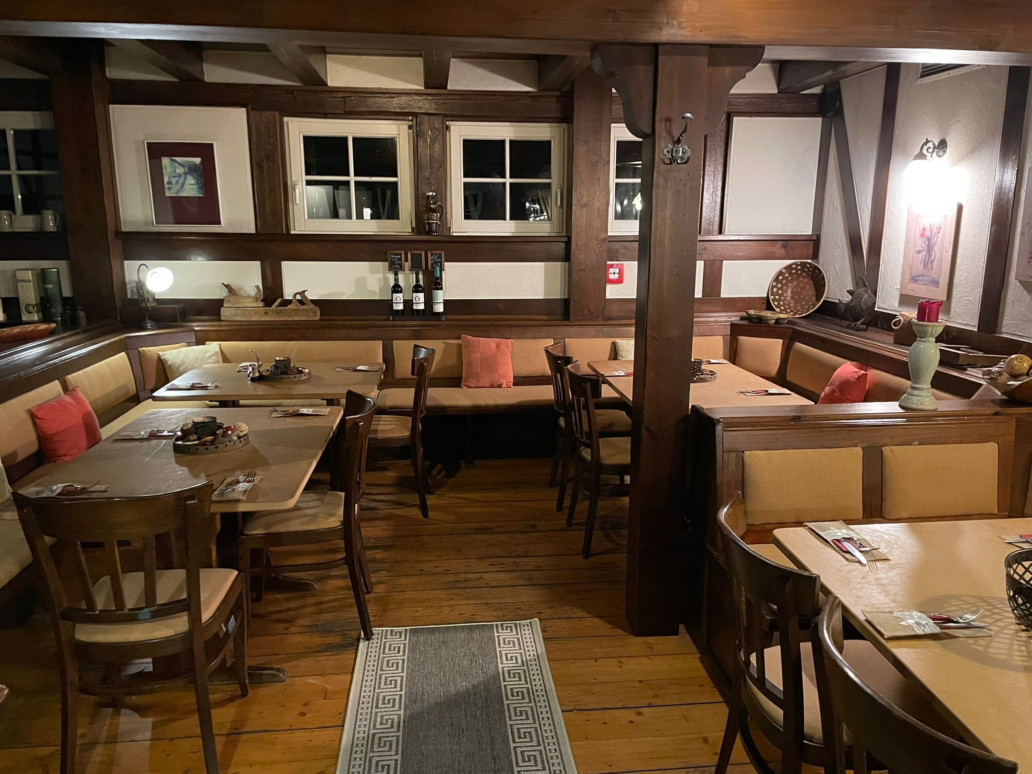 A cozy restaurant with wooden furniture, a patterned rug, and a variety of dishes on the tables.