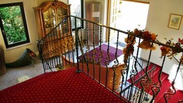 Una escalera con alfombra roja, una silla de madera y un barandal decorativo.