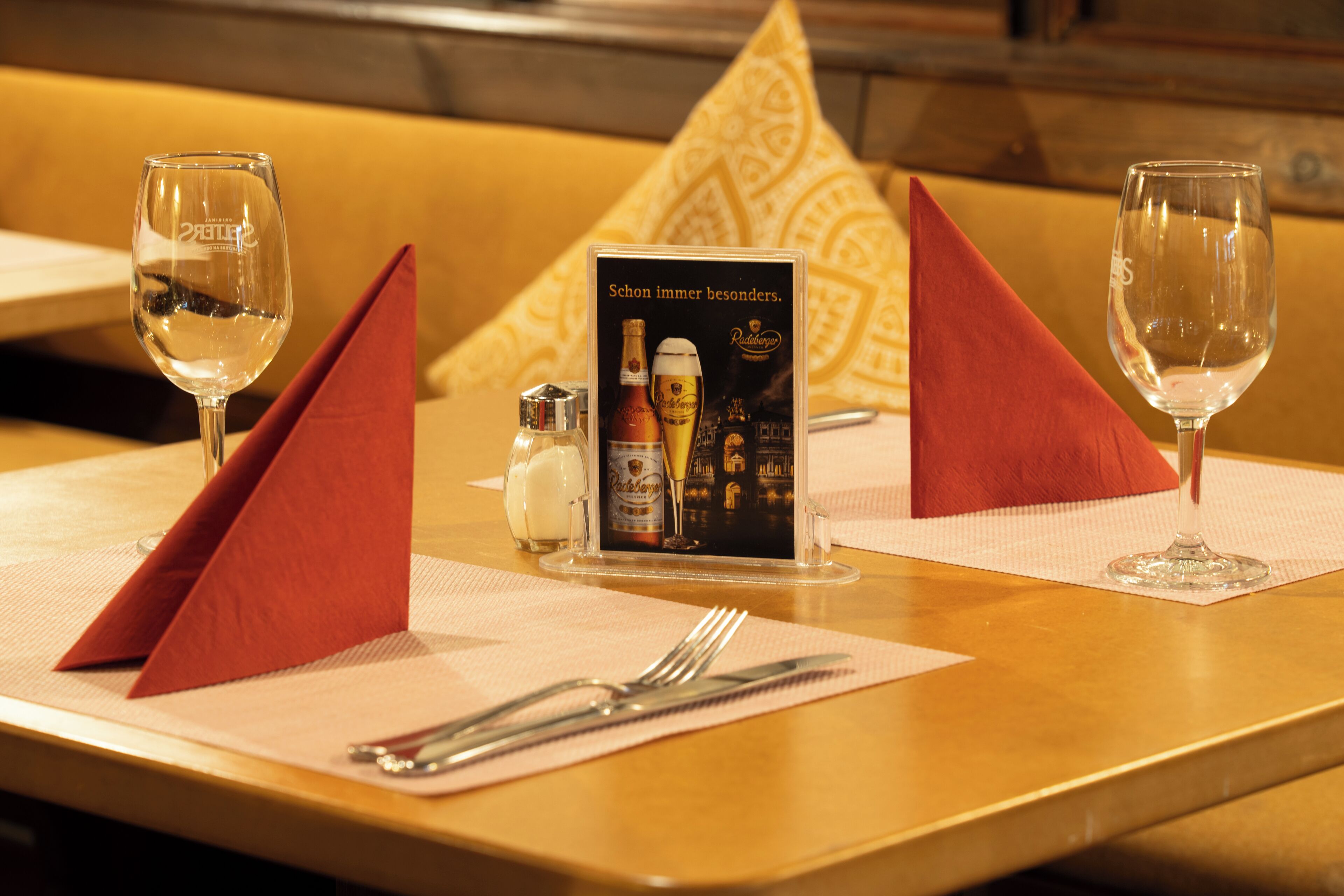 A hotel dining table set with a menu, two wine glasses, and a bottle of beer.