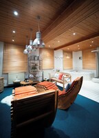 Quarto com teto e paredes de madeira, cama em forma de barco de madeira, uma mesa redonda e uma prateleira com toalhas.