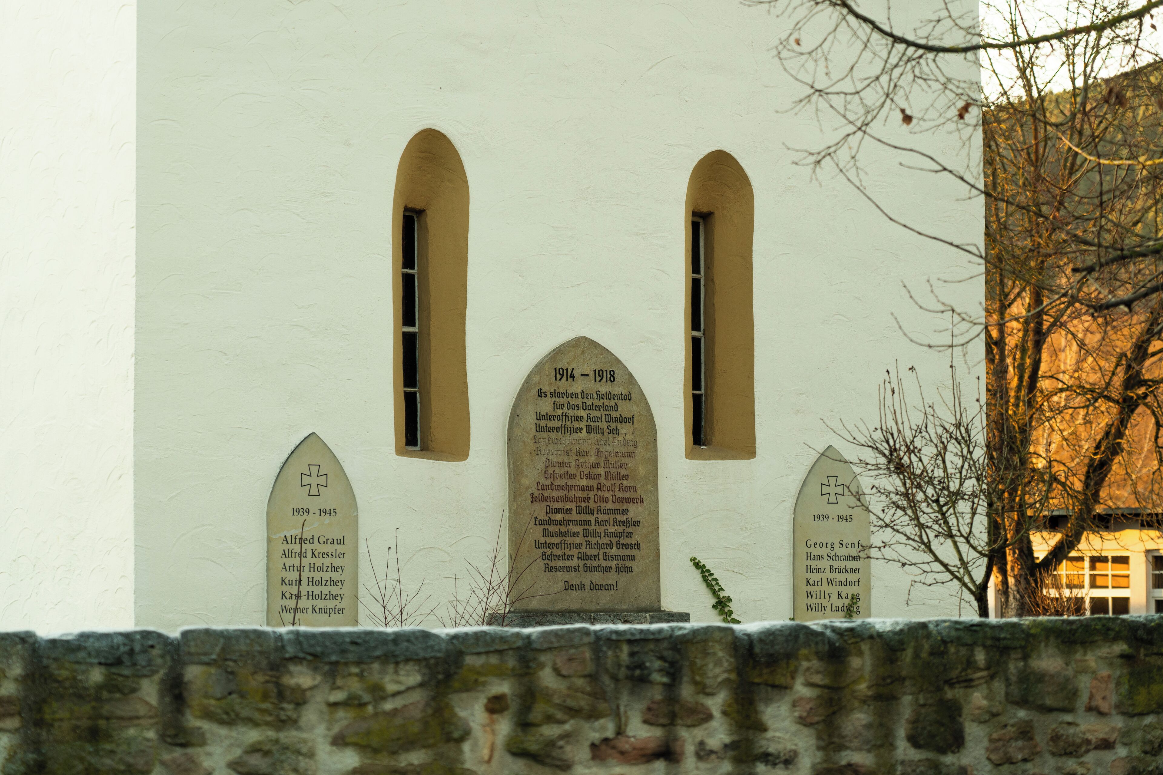 Een gebouw met drie stenen plaquettes op de gevel, elk met namen en data, wat wijst op herdenkingen of historische betekenis.