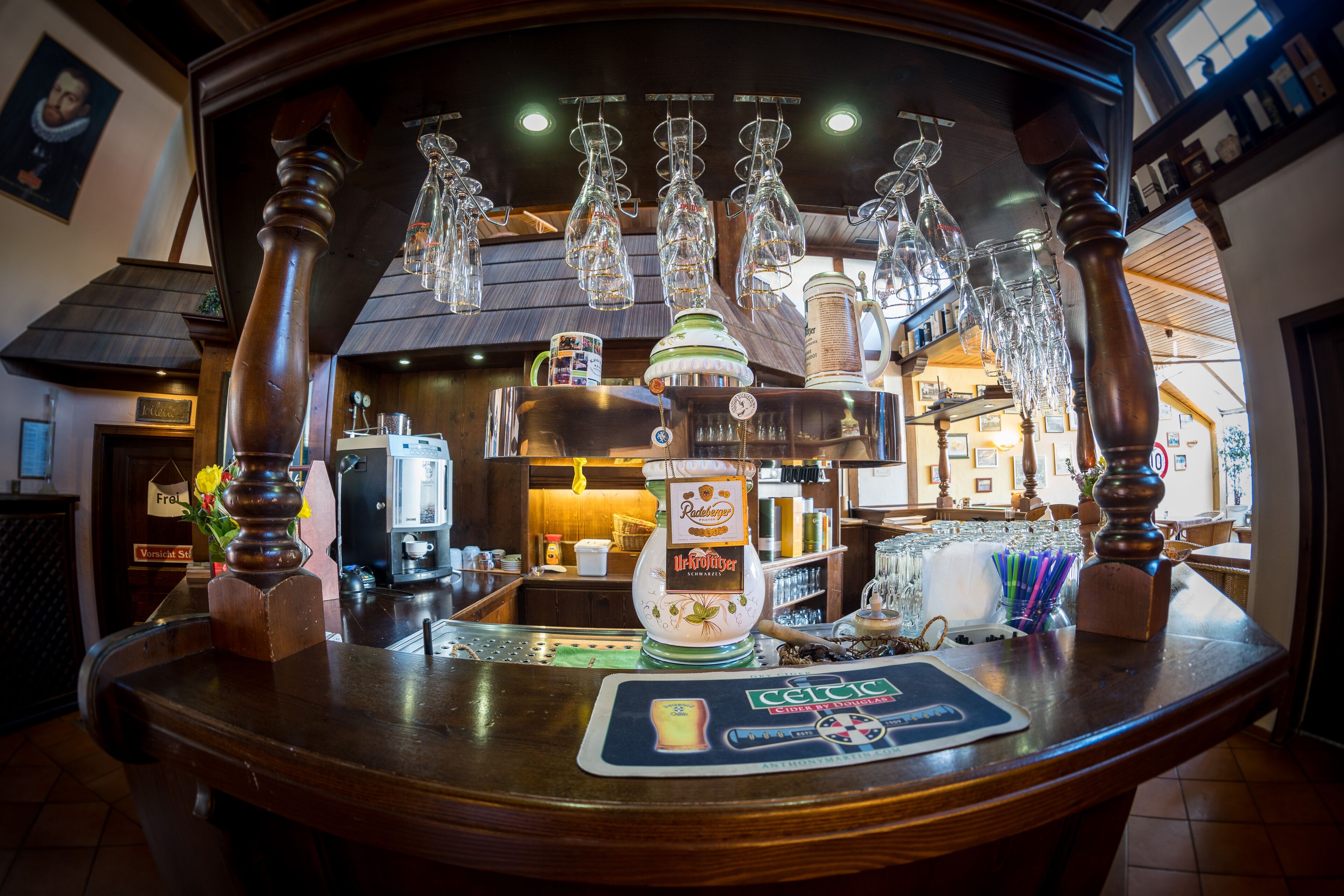 Una zona de bar con mostrador de madera, grifo de cerveza y copas colgantes.