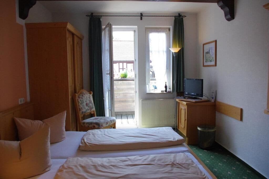 A room with two beds, a chair, a desk with a computer, and a window with curtains.