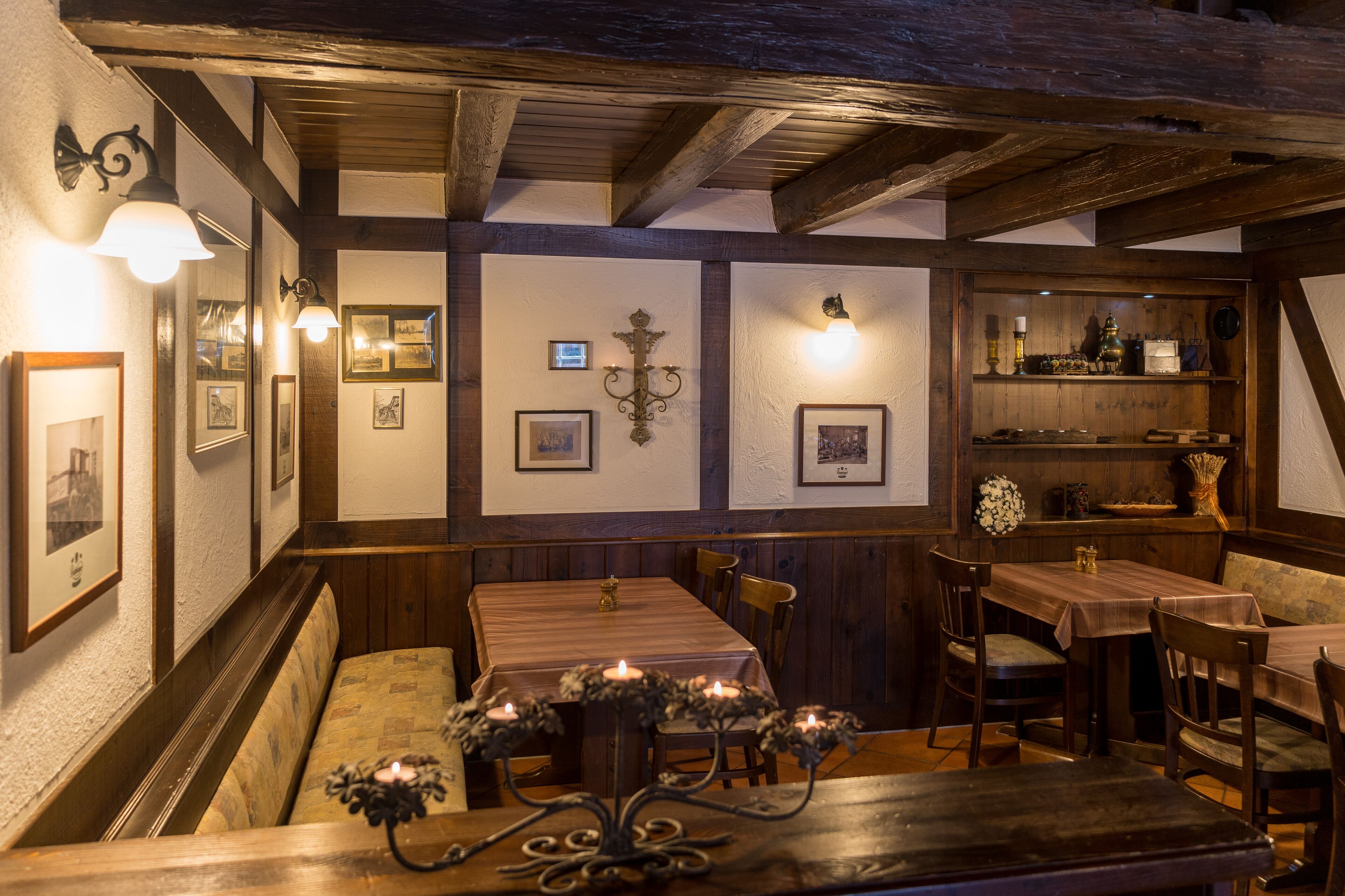 A cozy dining area with wooden tables and benches, framed pictures on the walls, and a chandelier.