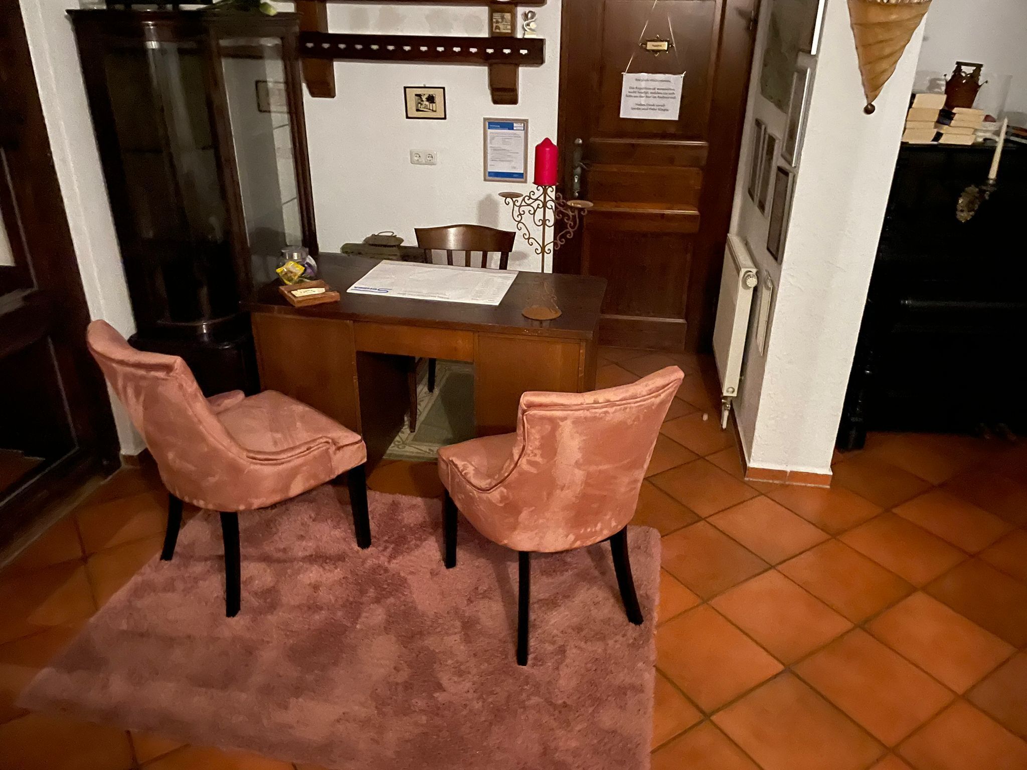 Un coin repas avec une table en bois, deux chaises roses, un tapis, et un espace cuisine comprenant un réfrigérateur et une cuisinière.