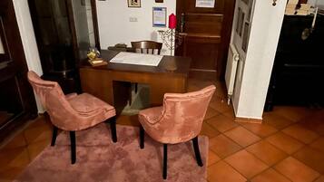 Un coin repas avec une table en bois, deux chaises roses, un tapis, et un espace cuisine comprenant un réfrigérateur et une cuisinière.