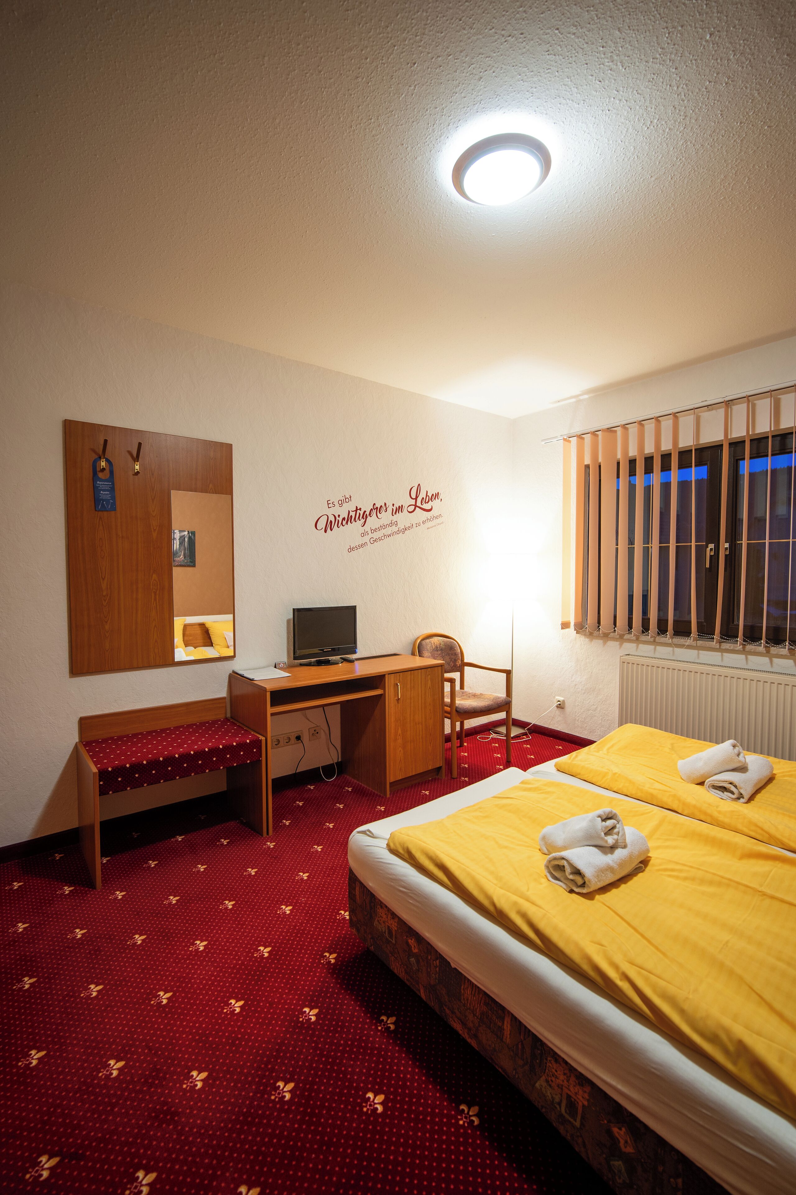 Une chambre d’hôtel avec un lit, un bureau, une chaise et un miroir au mur.