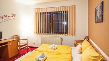 A hotel room with a bed, a desk, a chair, a radiator, and a window with bars.