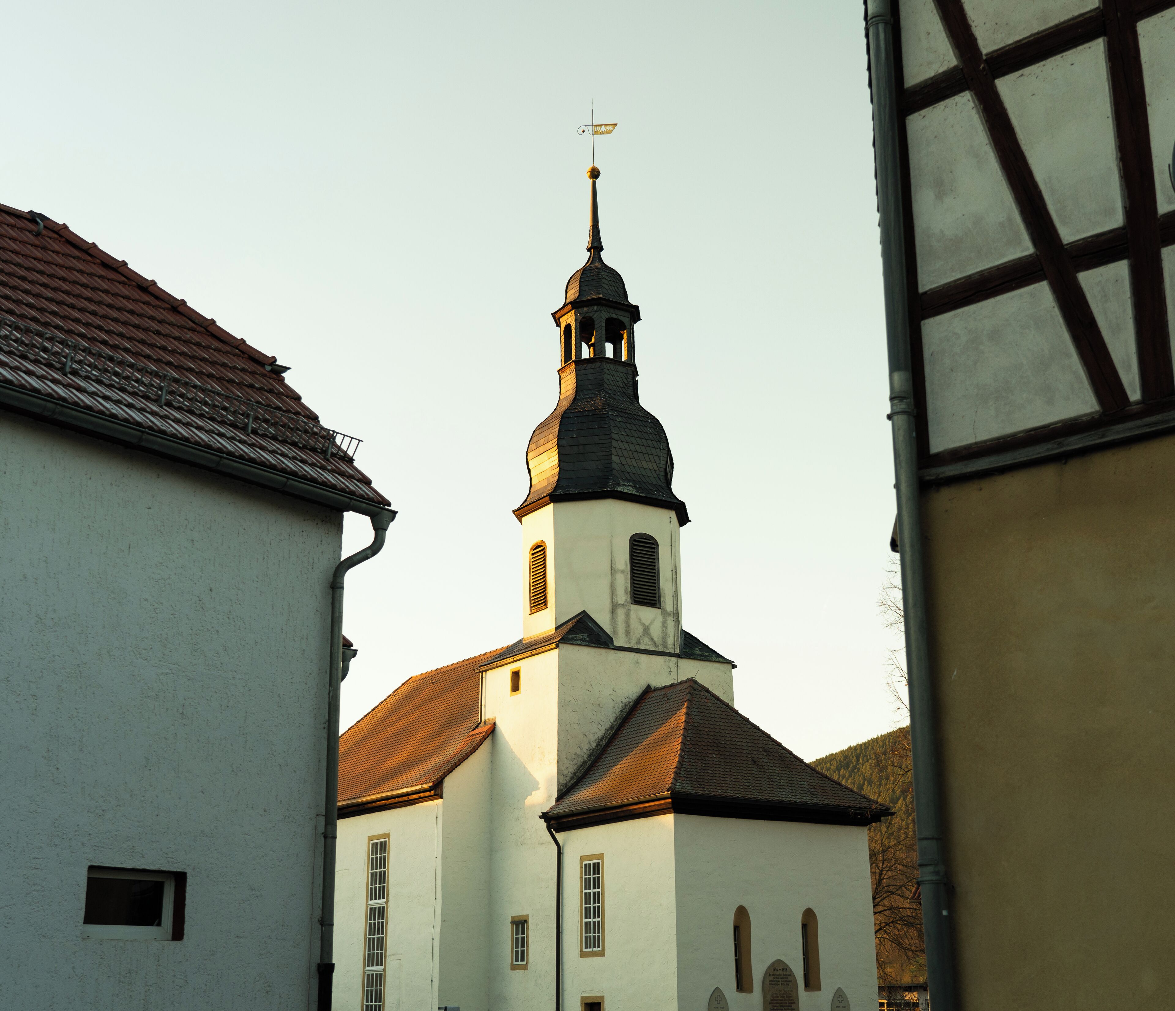 Una iglesia con un campanario destacado y una torre del reloj, rodeada de edificios tradicionales con fachadas blancas y tejados de tejas rojas.