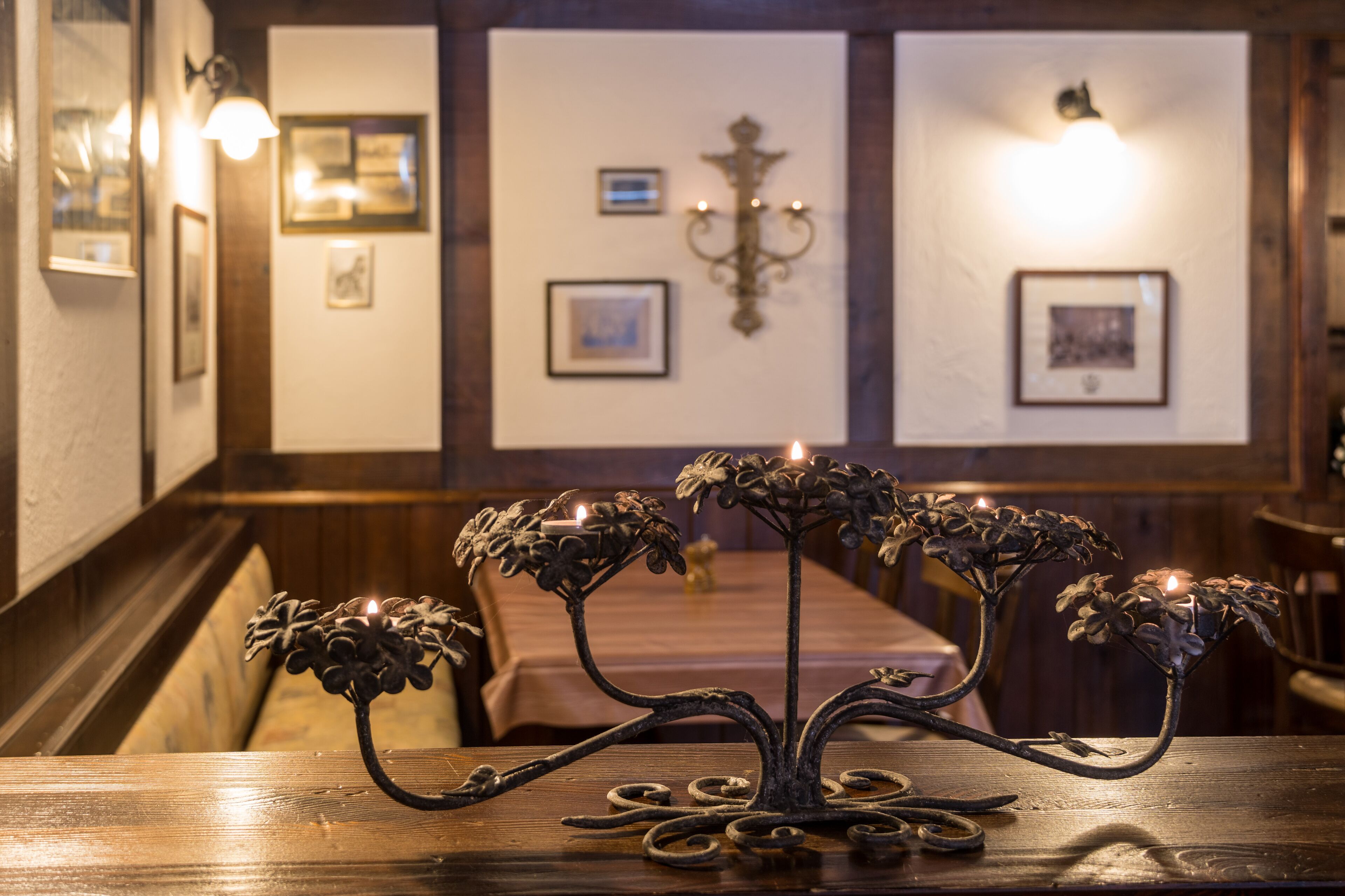 A candle holder on a wooden table in a room with framed pictures on the walls and a chandelier.