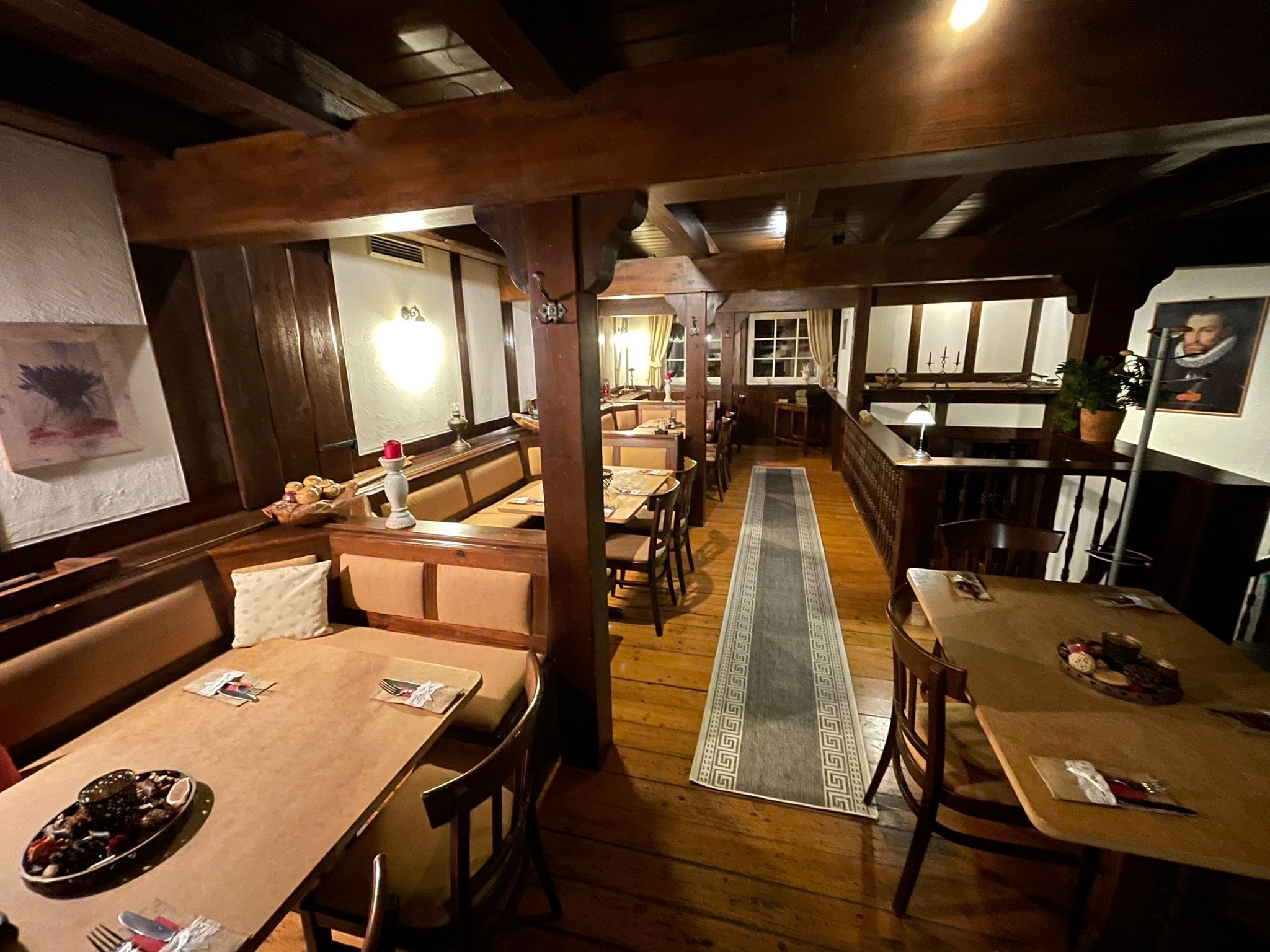 Un restaurant avec des tables et des bancs en bois, une longue allée centrale et un tapis décoratif.