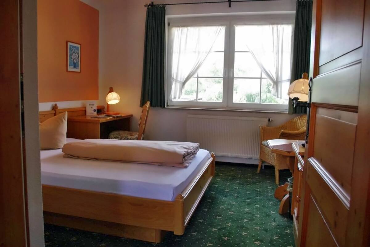 Un dormitorio con cama, mesita de noche, silla, ventana con cortinas y radiador.