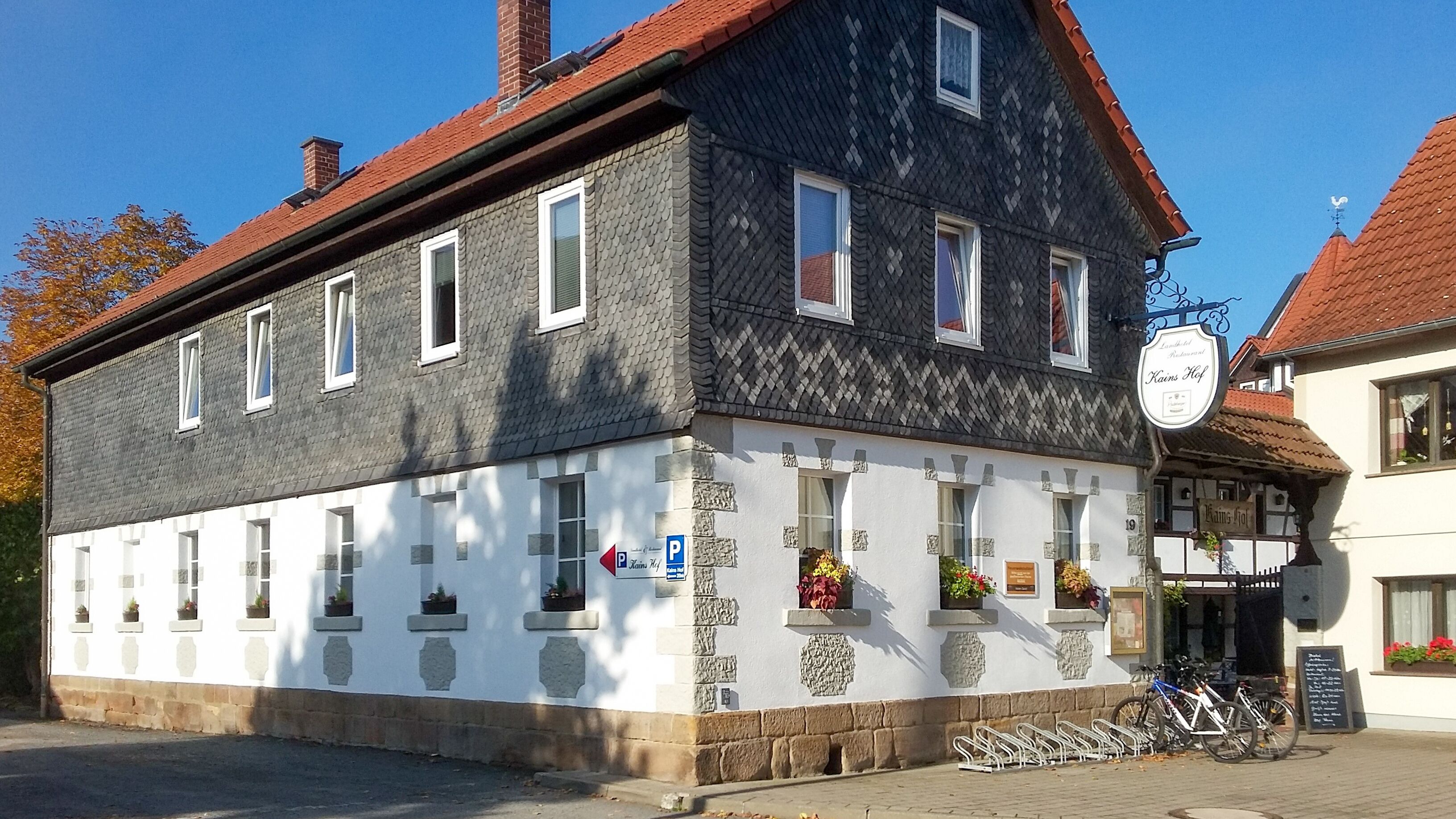 Un edificio de dos pisos con fachada blanca y techo oscuro. Tiene varias ventanas y un letrero que indica un restaurante.