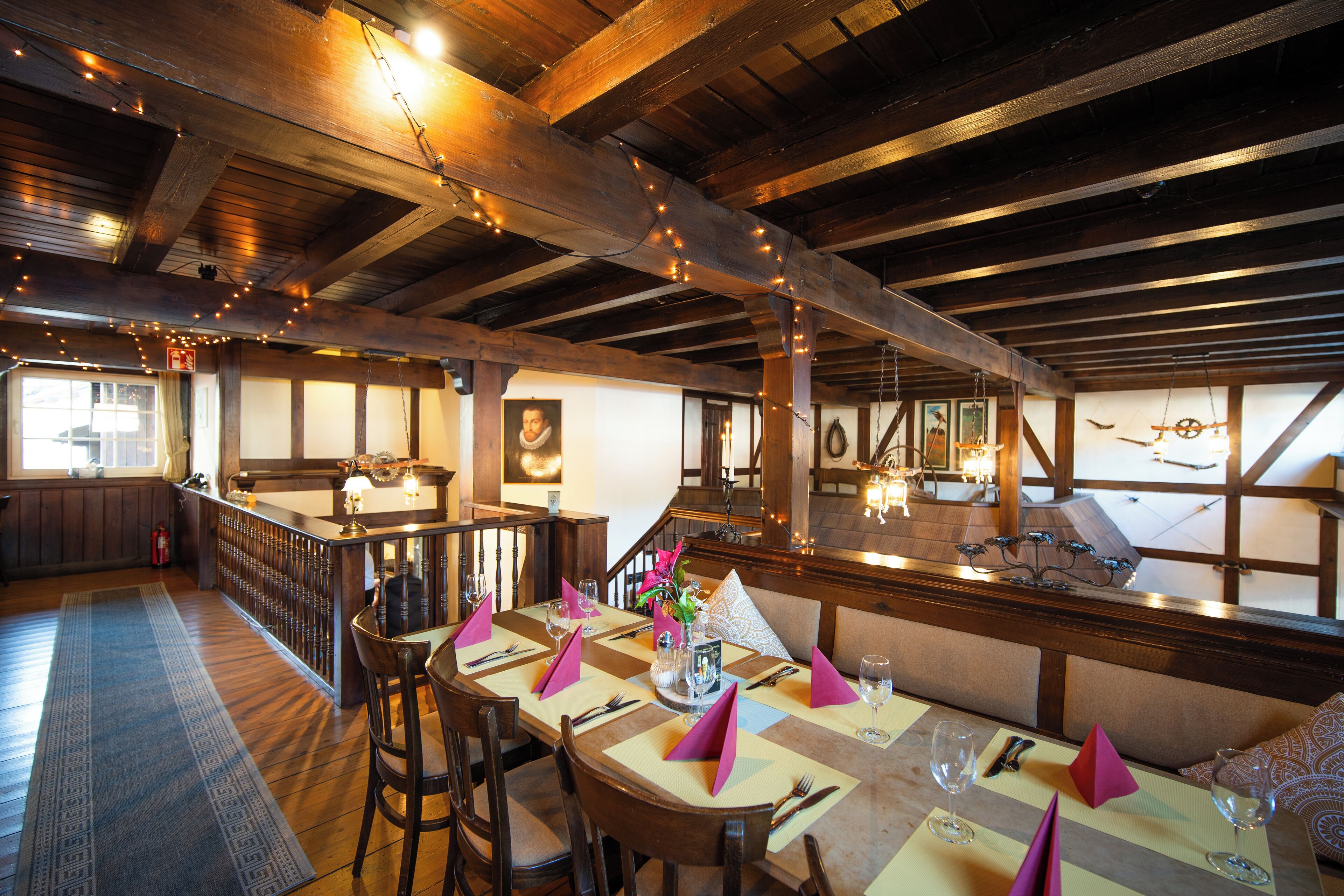 A dining area with wooden beams, string lights, and a view of the kitchen.