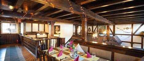 A dining area with wooden beams, string lights, and a view of the kitchen.