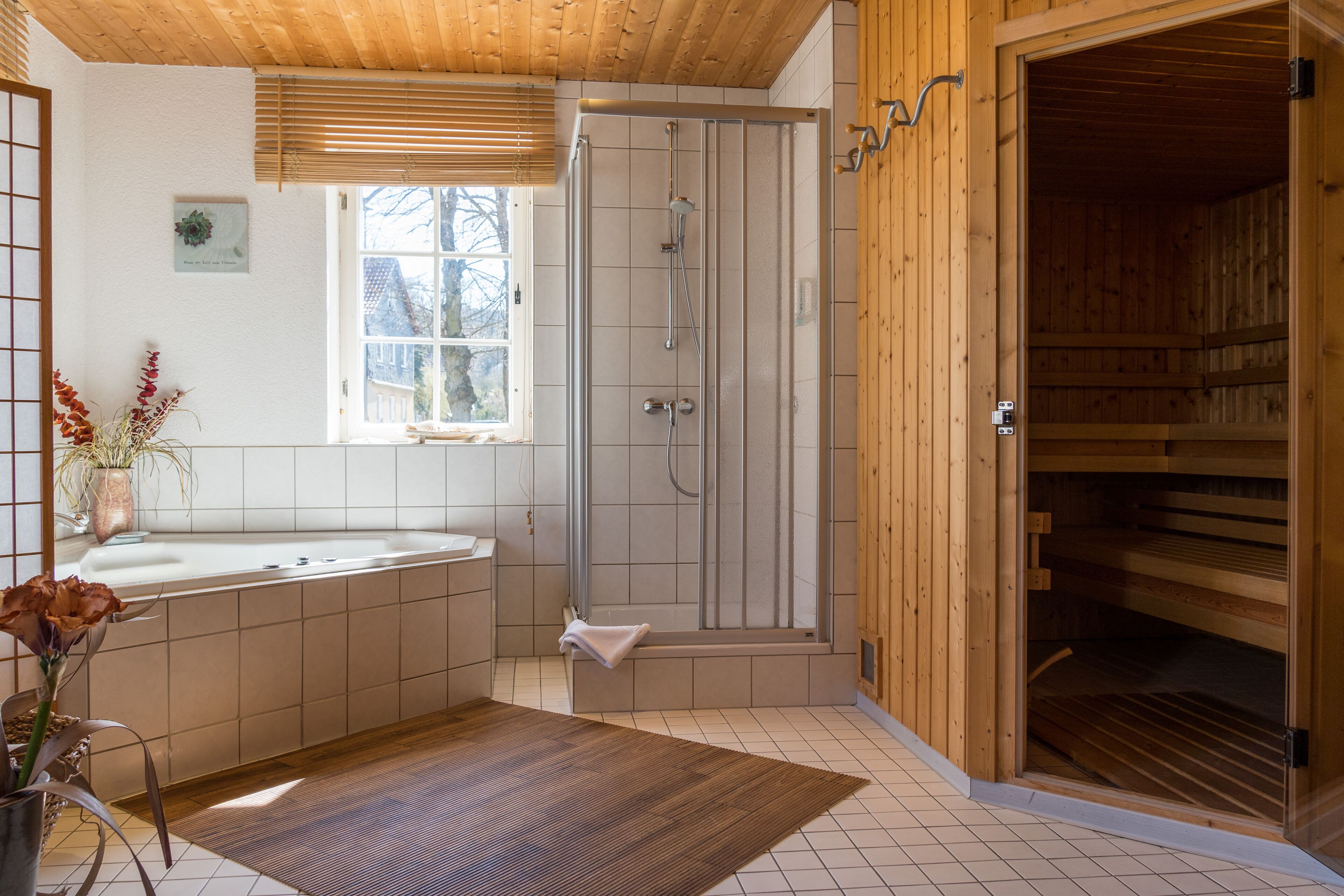 A modern bathroom with a wooden shower enclosure, a large bathtub, and a wooden sauna room.