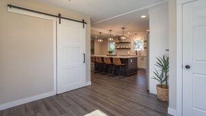 Une cuisine moderne dotée d’un îlot central, de tabourets de bar, de luminaires suspendus et d’une porte coulissante de style rustique.