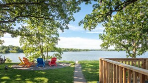 Une terrasse au bord du lac, dotée d’une rambarde en bois, d’un chemin en béton et de chaises Adirondack colorées, toutes orientées vers le lac, dont les eaux sont calmes.