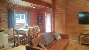 L’intérieur d’un chalet confortable, avec une salle à manger, un canapé et un téléviseur fixé au mur.