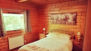 Une chambre à coucher dans une cabane en bois, avec un lit, deux tables de chevet avec des lampes, un radiateur et une fenêtre avec des rideaux.