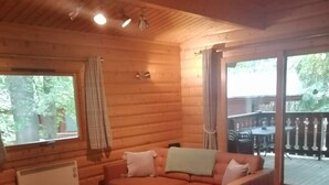L’intérieur d’un chalet confortable, avec un grand canapé, une table basse en bois et une vue sur l’extérieur grâce à une porte-fenêtre coulissante.