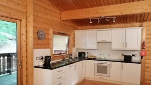 L’intérieur d’une cabane en bois comprend une cuisine avec des meubles blancs, un plan de travail noir et un plafond en bois.