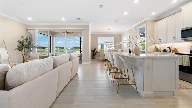 A spacious living area with a large sofa, a dining area with bar stools, and a kitchen with white cabinets and a large island.