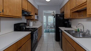A narrow kitchen with wooden cabinets, a black stove, a microwave, and a refrigerator. - Charming Townhouse - great walkable area 5 min from Downtown (Columbus)